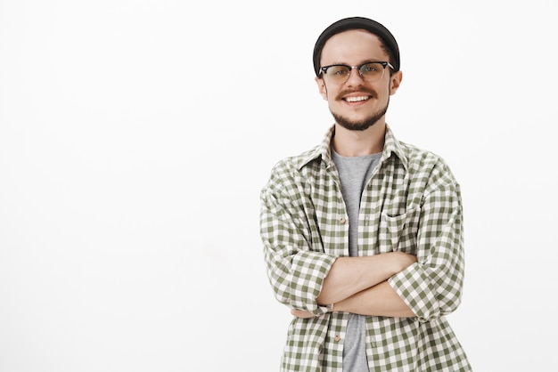 Foto gratuita hábil e inteligente apuesto hombre europeo con gorro negro y camisa verde a cuadros, sonriendo con expresión segura de sí misma y lograda, sonriendo ampliamente, satisfecho con el trabajo bien hecho