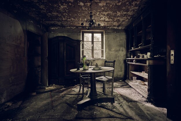 Habitación abandonada con una mesa en el medio y estantes contra una pared cerca de la ventana.