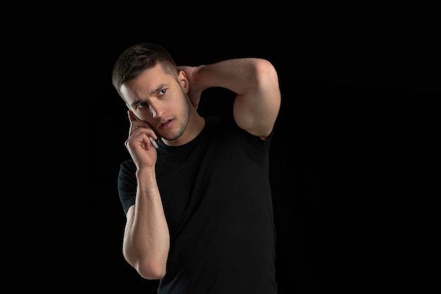 Hablando por telefono. Retrato monocromo de joven caucásico aislado en pared negra. Hermoso modelo masculino. Las emociones humanas, la expresión facial, las ventas, el concepto publicitario. Cultura juvenil.