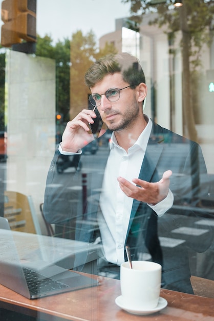 Foto gratuita el hablar gesticular del hombre de negocios joven en el teléfono elegante en café