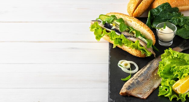 Hacer un sándwich de filete de arenque con cebolla, pepino y ensalada en una tabla de piedra