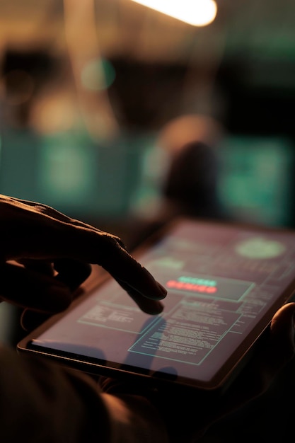 Un hacker afroamericano sostiene una tableta para hackear un sistema en línea, causando malware en la red y planeando un ciberataque. Mirando el servidor de seguridad para acceder a la base de datos y robar contraseñas.