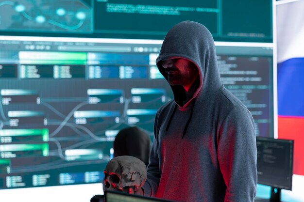 Hacker fuera de la ley digital con una capucha oscura emitiendo amenazas cibernéticas con un cráneo humano