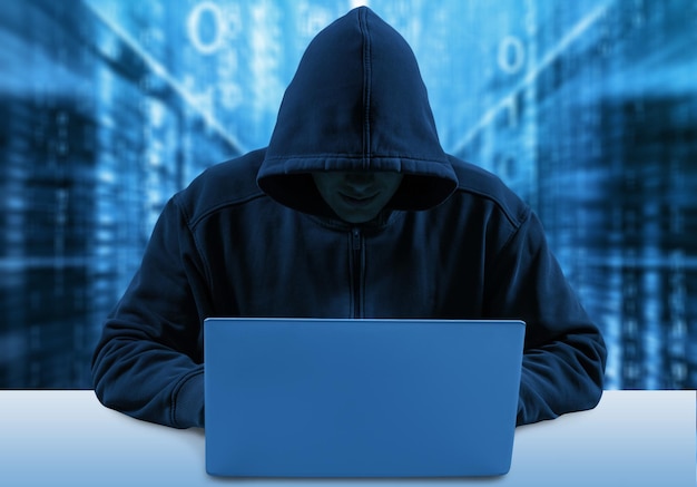 Hacker indefinido usando computadora con sudadera con capucha oscura