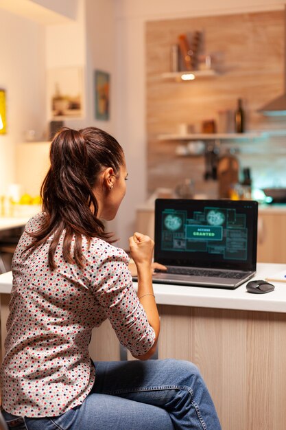 Hacker de mujer feliz después de romper el firewall del gobierno y obtener acceso. Programador que escribe un malware peligroso para ataques cibernéticos utilizando una computadora portátil de rendimiento durante la medianoche.