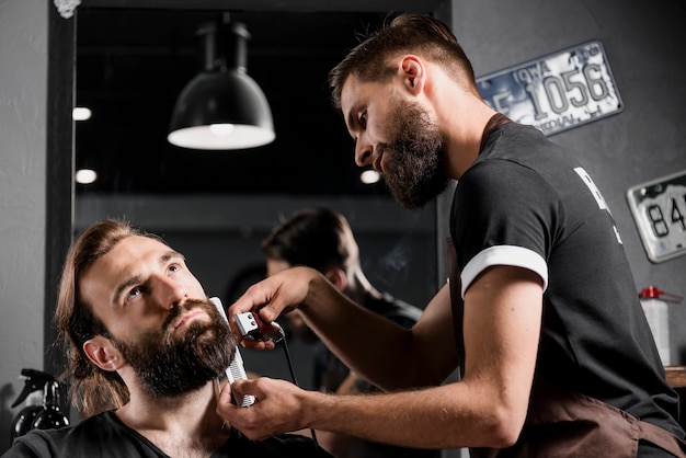 Hairstylist corte la barba del hombre en peluquería