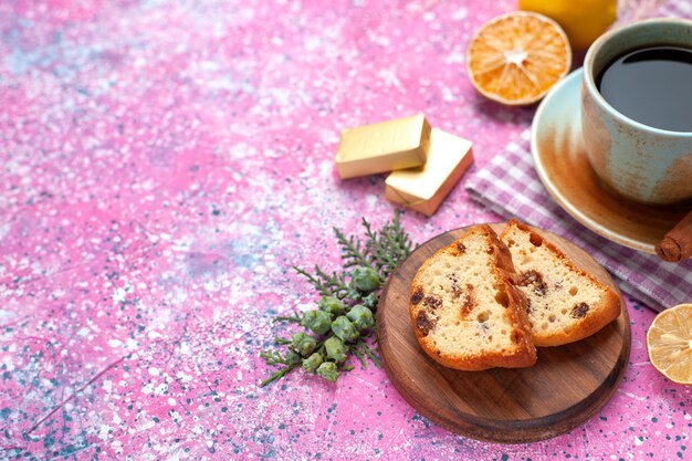 Half-top close view delicioso pastel en rodajas con una taza de té, canela y limones en el escritorio rosa claro.