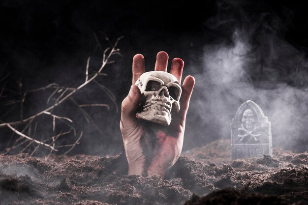 Halloween zombie mano sosteniendo el cráneo en el cementerio