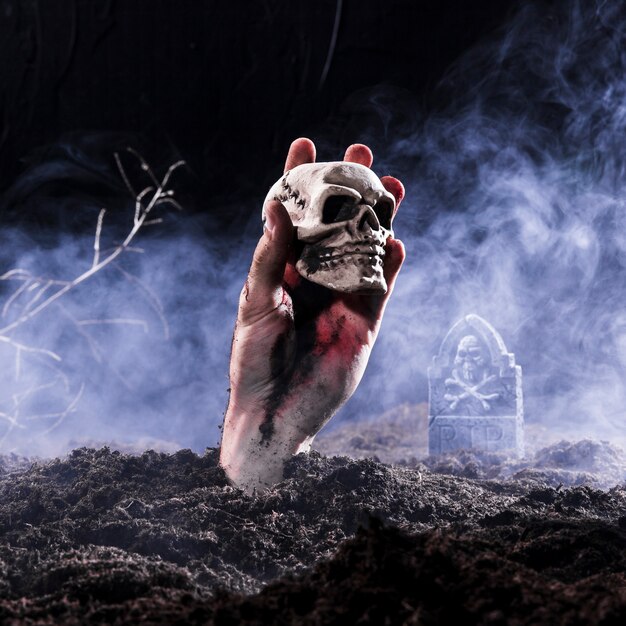 Halloween zombie mano sosteniendo el cráneo en el cementerio