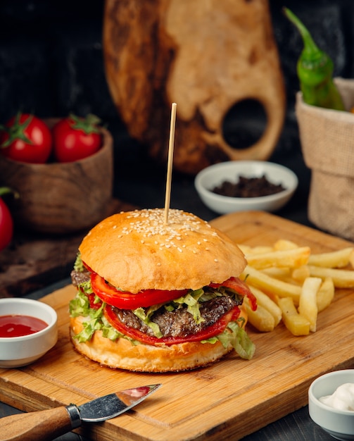 Hamburguesa en bollo de pan con patatas en una tabla de madera.