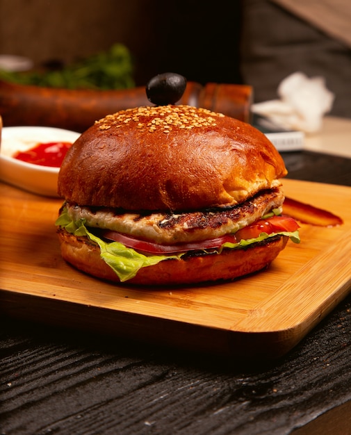 Hamburguesa de carne de pollo con rodajas de tomate y lechuga servida con salsa de tomate y mayonesa sobre tabla de madera