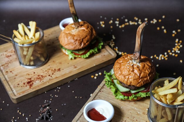 Hamburguesa de carne en el tablero de madera lechuga tomate pepino papas fritas vista lateral