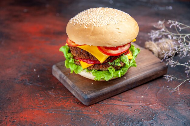 Hamburguesa de carne vista frontal con ensalada de queso y tomates en el fondo oscuro