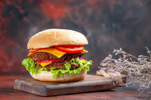 Hamburguesa de carne vista frontal con ensalada de queso y tomates en el fondo oscuro