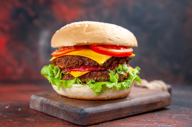 Hamburguesa de carne vista frontal con ensalada de queso y tomates en piso oscuro