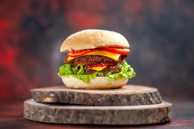 Hamburguesa de carne vista frontal con ensalada de queso y tomates sobre fondo oscuro