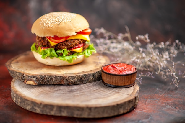 Hamburguesa de carne vista frontal con ensalada de queso y tomates sobre fondo oscuro