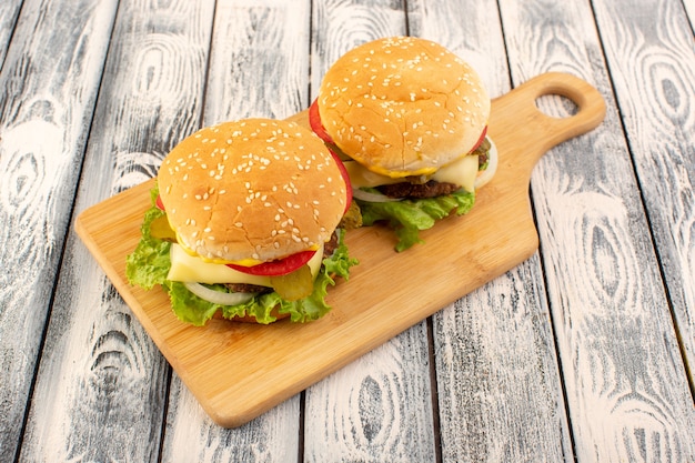 Foto gratuita una hamburguesa de carne de vista frontal con queso y ensalada verde en la mesa de madera y mesa gris