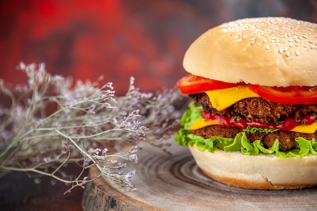 Hamburguesa de carne vista frontal con queso, tomates y ensalada sobre fondo oscuro