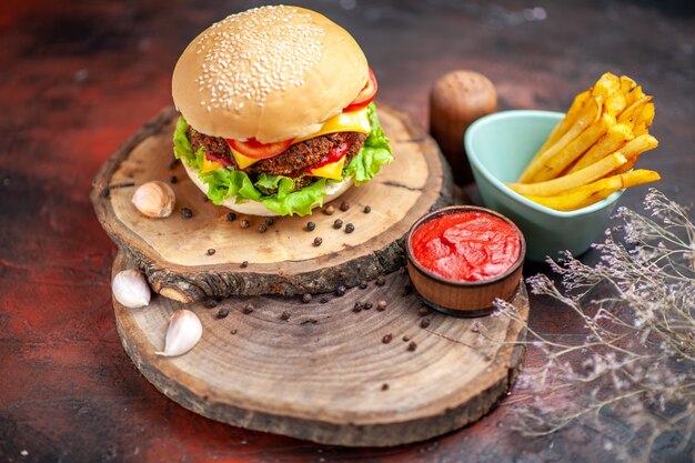 Hamburguesa de carne vista frontal con tomate, queso y ensalada sobre fondo oscuro