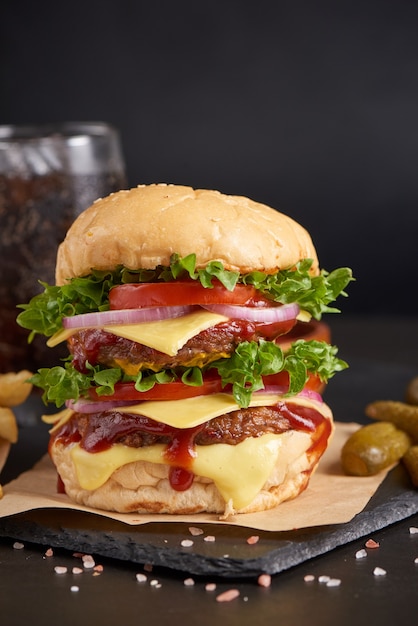 Hamburguesa casera o hamburguesa con verduras frescas y queso, lechuga y mayonesa servida, papas fritas en trozos de papel marrón sobre una mesa de piedra negra. concepto de comida rápida y comida chatarra.