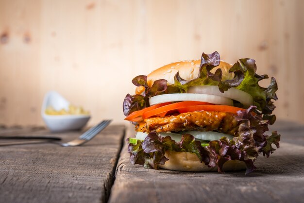 Hamburguesa casera de pollo con papas fritas, lechuga, tomate y cebolla en tabla de madera.