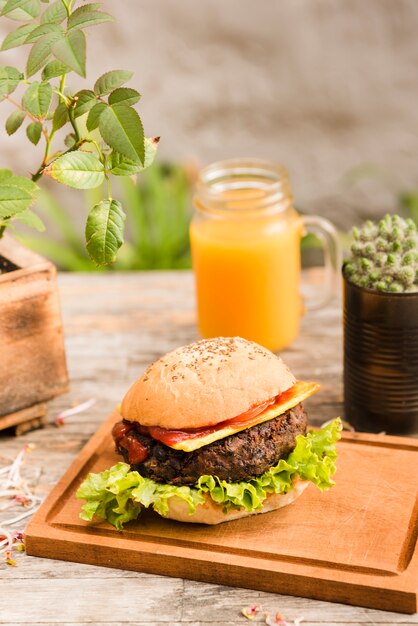 La hamburguesa deliciosa en la tajadera sirvió con el tarro del jugo en el escritorio de madera