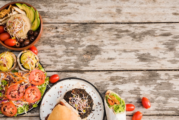 Hamburguesa; ensalada; Envoltura de burrito y tazón de fuente con tomates cherry sobre fondo con textura de madera