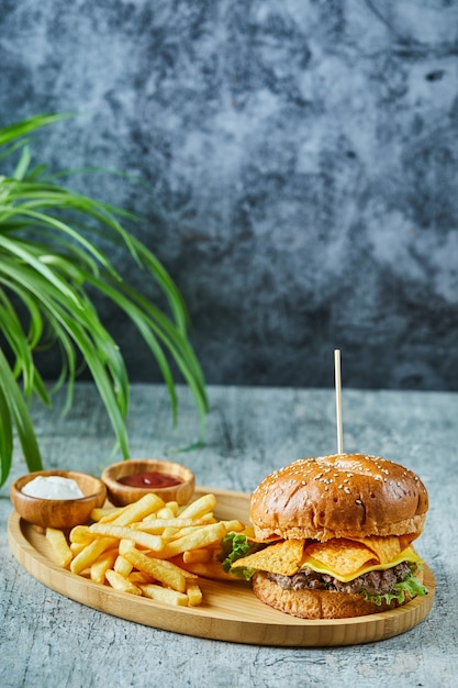 Hamburguesa grande con patatas fritas en la placa de madera sobre la superficie de mármol