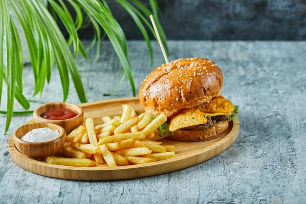 Hamburguesa grande con patatas fritas en la placa de madera sobre la superficie de mármol