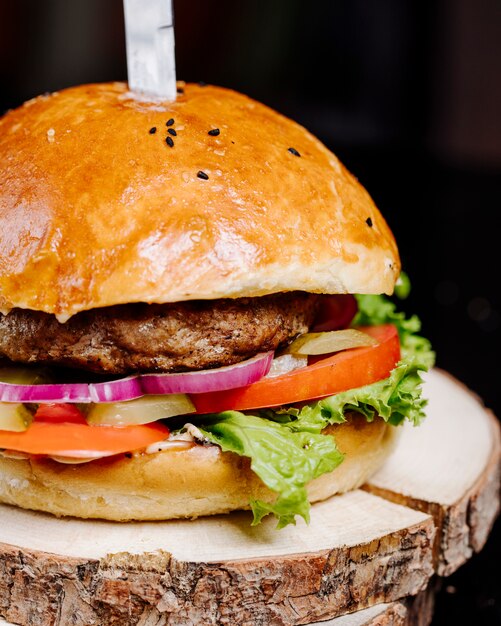 Una hamburguesa en pan bollo con cuchillo en una pieza de madera.