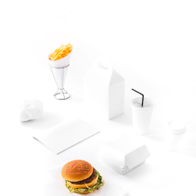 Hamburguesa; papas fritas; Paquete desechable de bebidas y papel sobre fondo blanco.