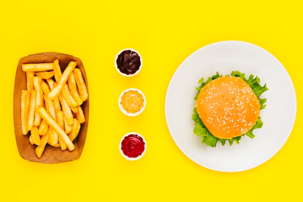 Hamburguesa plana con papas fritas y salsas.