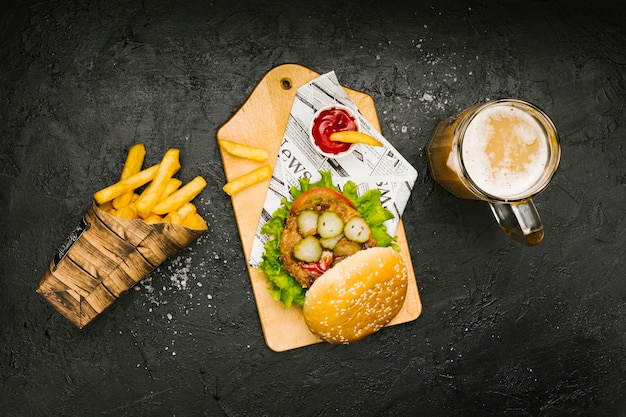 Hamburguesa plana sobre tabla de madera con papas fritas y cerveza.