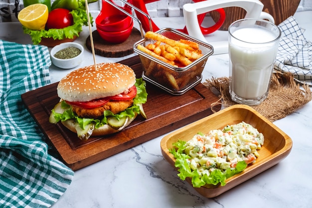 Hamburguesa de pollo con papas fritas en un tablero, una ensalada capital y un vaso de yogurt