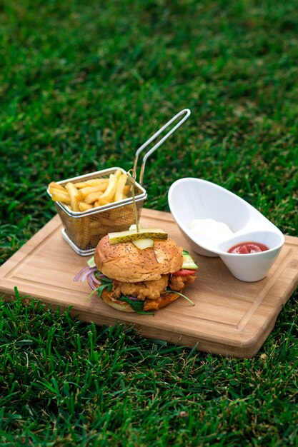 Hamburguesa de pollo servida con canasta de papas fritas, tazón de mayonesa y salsa de tomate