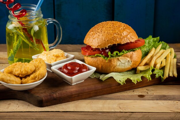 Hamburguesa, rollos de cebolla y papas fritas con salsas y tomates servidos con un vaso de jugo.