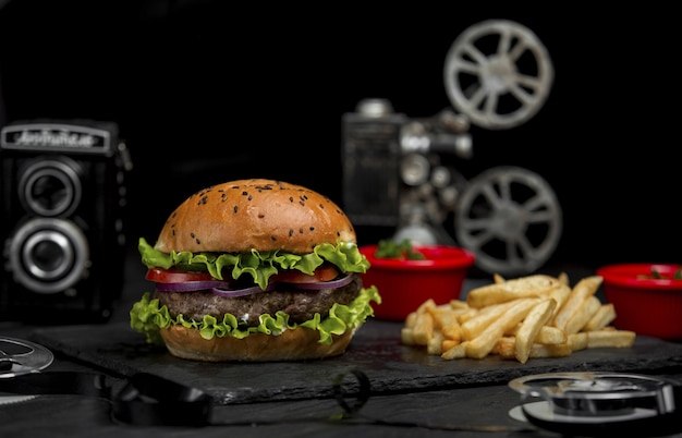 Hamburguesa de ternera con cebolla picada y tomates dentro del pan y con papas fritas en una fuente de piedra