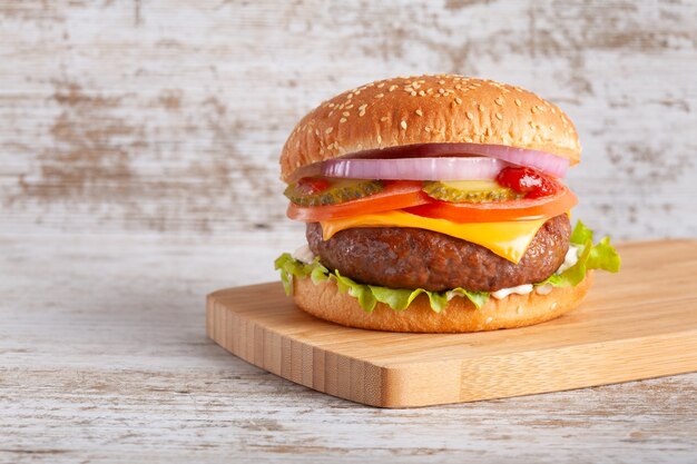 Hamburguesa con tomate, queso, cebolla, lechuga y pepinillo sobre tabla de madera