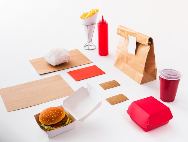 Hamburguesa; vaso desechable; botella de salsa; Papas fritas y paquete de comida sobre fondo blanco