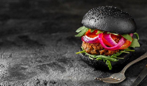 Hamburguesa vegetariana vista frontal con bollos negros sobre tabla de cortar con espacio de copia