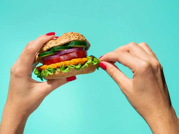 Hamburguesa de verduras en la mano sobre un fondo azul.