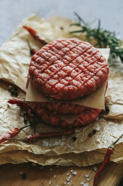 Foto gratuita hamburguesas de carne cruda con hierbas y especias en placa de pizarra oscura