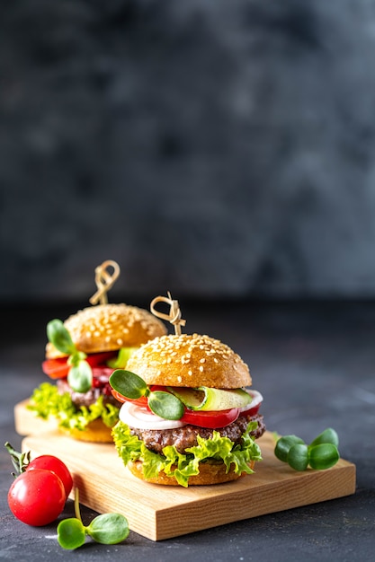 Hamburguesas con chuleta de carne, lechuga fresca, tomates, cebollas en una piedra oscura. copia espacio