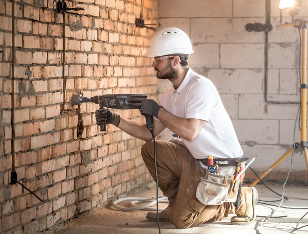 Handyman utiliza martillo neumático, para la instalación, trabajador profesional en el sitio de construcción. El concepto de electricista y personal de mantenimiento.