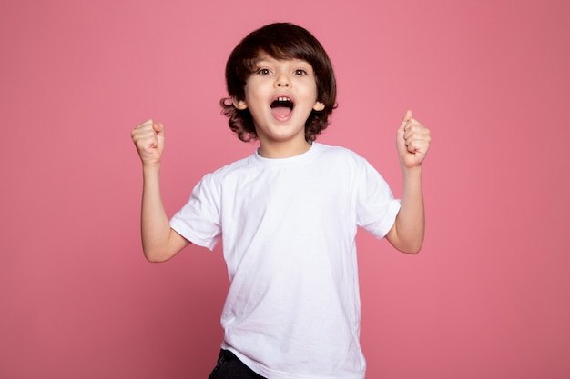 Happy boy little cute adorable en camiseta blanca y jeans azul sobre rosa