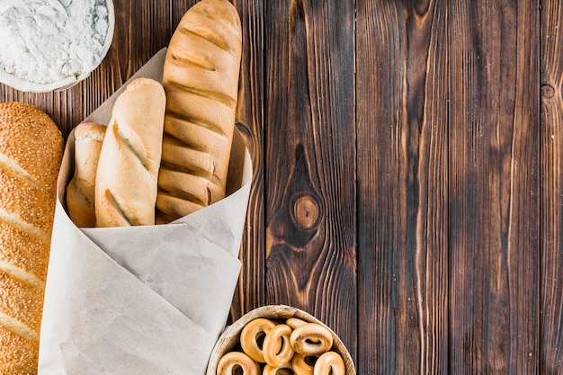 Harina, baguettes y panecillos en el fondo de madera