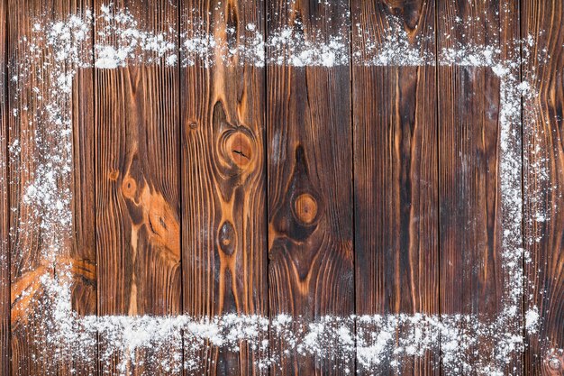 Harina blanca sobre el borde del marco rectangular en la mesa de madera