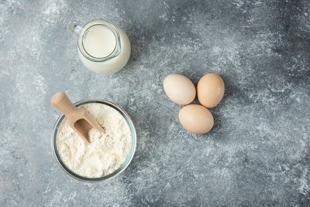 Harina, huevos crudos y leche sobre mármol.