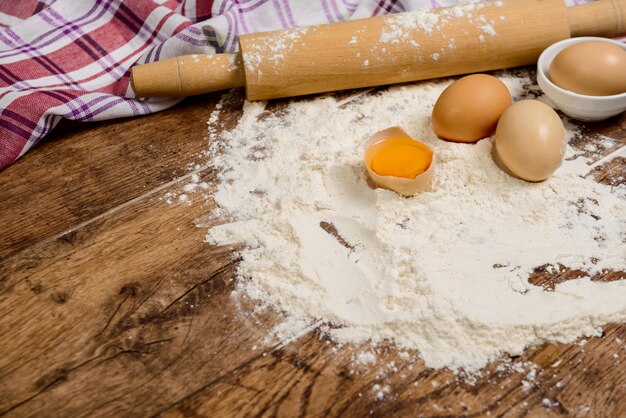 Harina, huevos, sal, toalla, rodillo sobre una mesa de madera lista para cocinar